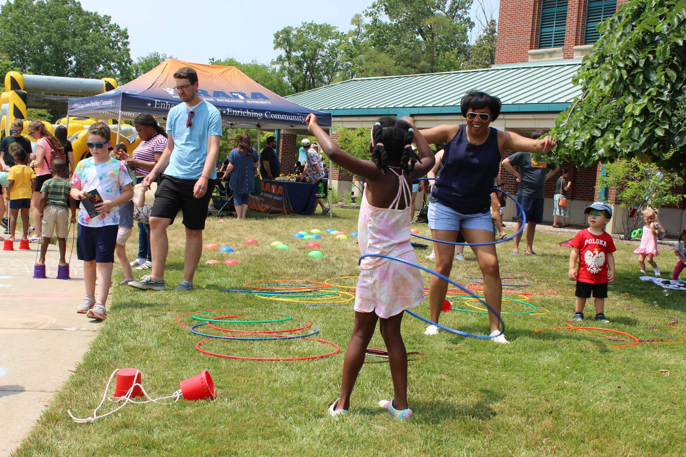 Patrons enjoying event with hula-hoops and bounce house outside the library